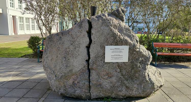Large cracked glacial erratic stone with commemorative plaque in an urban park.