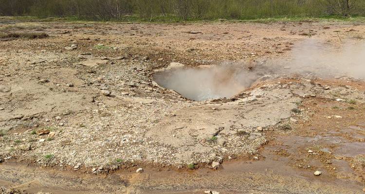 Small bubbling geothermal vent surrounded by mineral-rich soil at Geysir field.