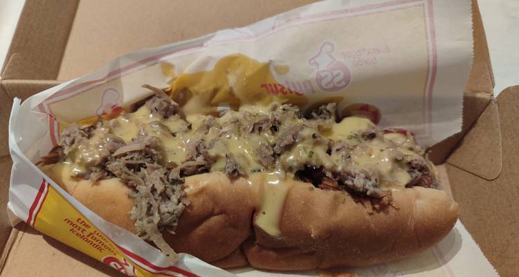 Icelandic hot-dog bun loaded with shredded lamb, mustard and creamy sauce in a takeaway box.