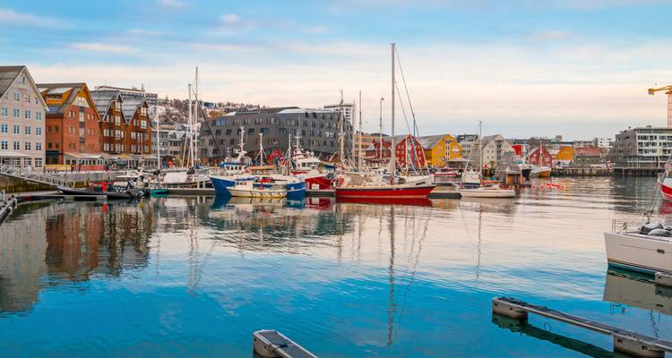 Port animé avec des bateaux de pêche et des bâtiments nordiques colorés se reflétant dans une eau calme.