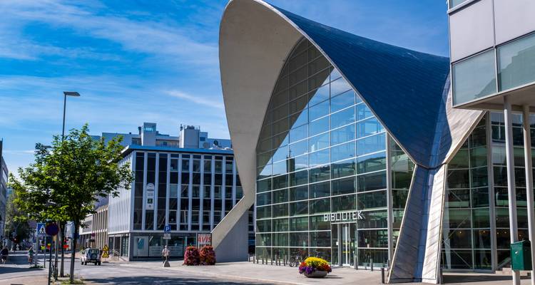 Bibliothèque aux façades vitrées modernes avec toit courbe élancé dans une rue urbaine ensoleillée.