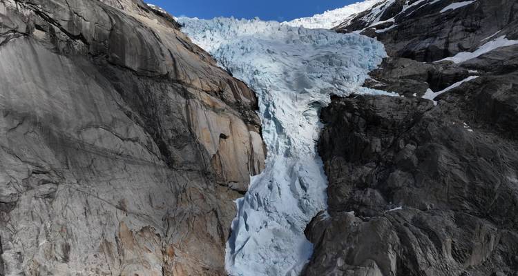 Paroi verticale de glace glaciaire brillante s'écoulant entre des parois rocheuses sombres.