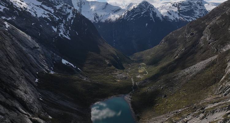 Bassin alpin élevé avec un lac turquoise reflétant les nuages sous des pics enneigés imposants.