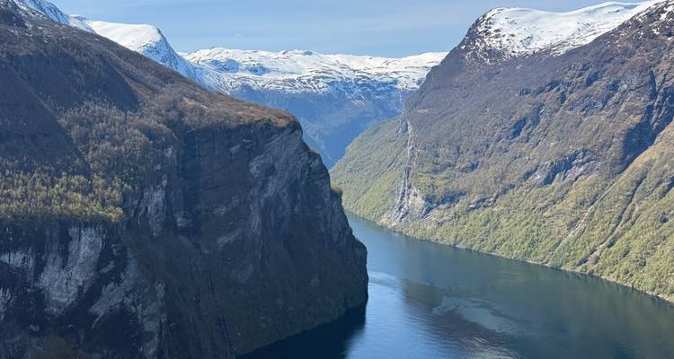 Fjord ensoleillé se découpant entre des falaises escarpées, boisées et couronnées de neige par une claire journée de printemps.