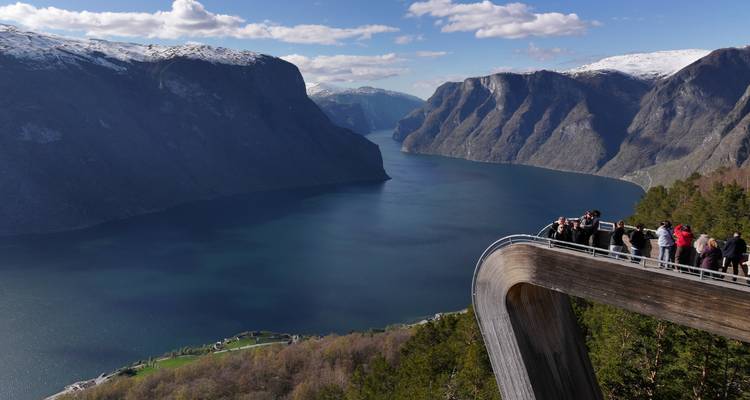 Les touristes se rassemblent sur la plateforme d'observation en bois incurvée de Stegastein, surplombant un profond fjord bleu encadré par des montagnes aux sommets enneigés.