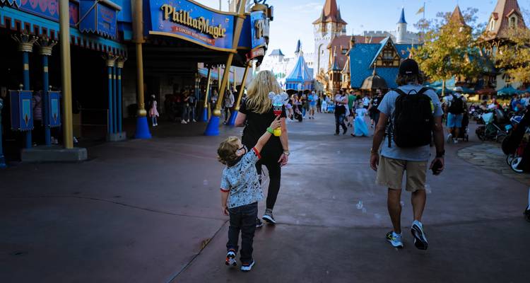 Rue animée à thème conte de fées dans un parc d'attractions où un petit garçon tient fièrement un jouet, entouré d'autres visiteurs.