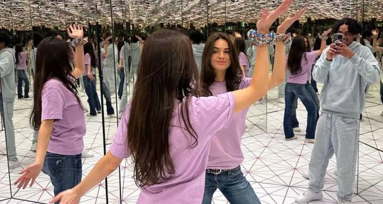 Salle de miroirs réfléchissants créant de multiples illusions de deux jeunes visiteurs dansant et prenant des photos.