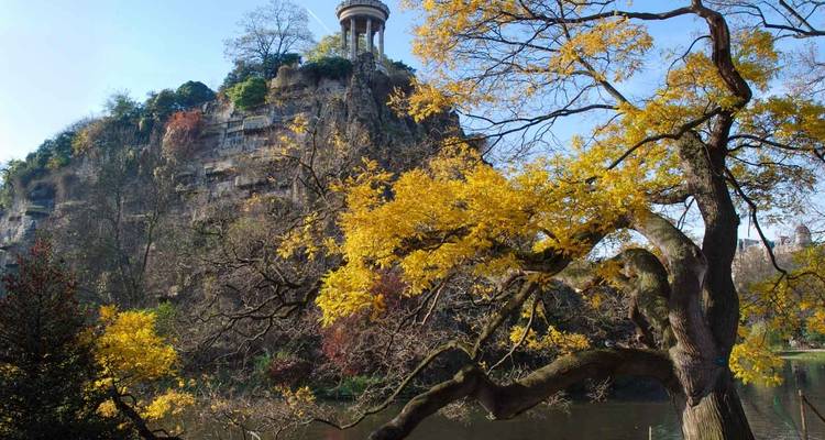 Colline rocheuse dramatique couronnée du Temple de la Sibylle surplombant un lac serein encadré par le feuillage automnal doré dans un parc parisien.