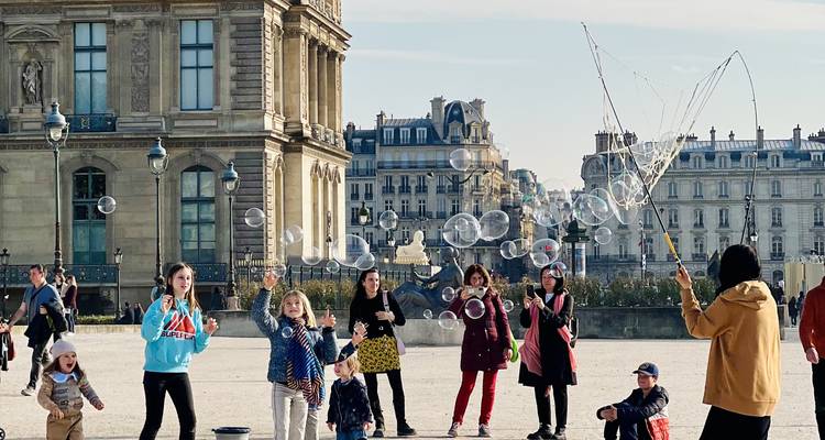 Les enfants et les adultes poursuivent avec joie des bulles de savon dans la cour du Louvre par une belle journée ensoleillée.