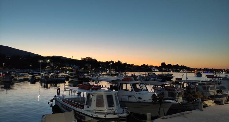 Harbor of small fishing boats at dusk with orange glow on the horizon.