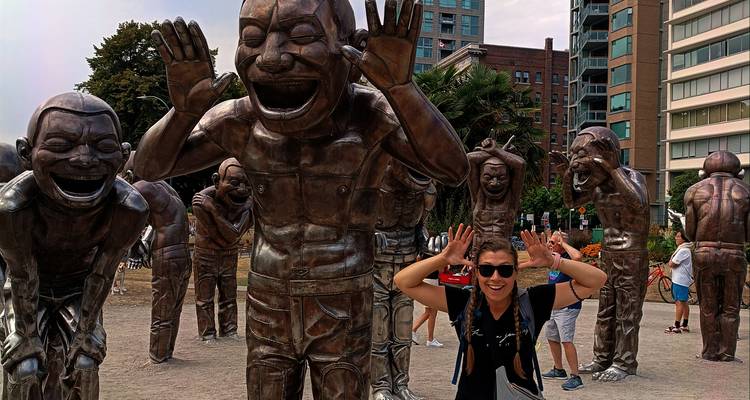 Traveler playfully posing with large bronze laughing statues in an urban park