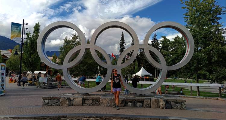 Visitors standing beneath the steel Olympic Rings monument in a mountain resort plaza