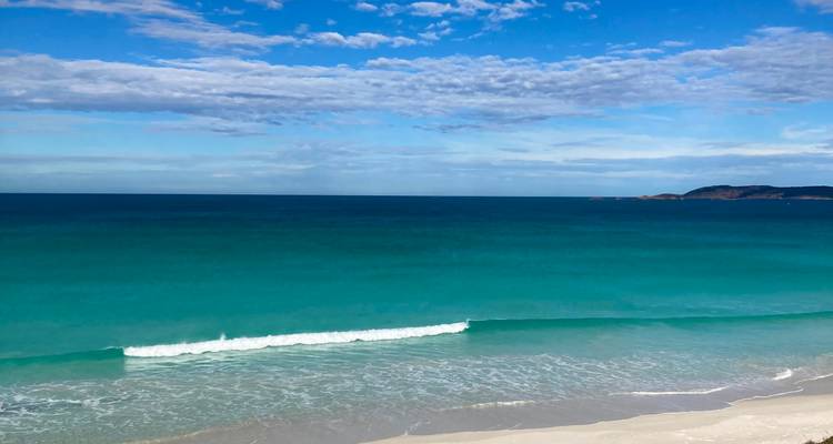 Emerald sea with a single gentle wave under a vast blue sky and distant headland
