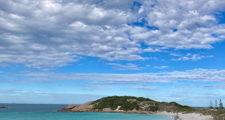Small rocky island and turquoise bay beneath patterned clouds