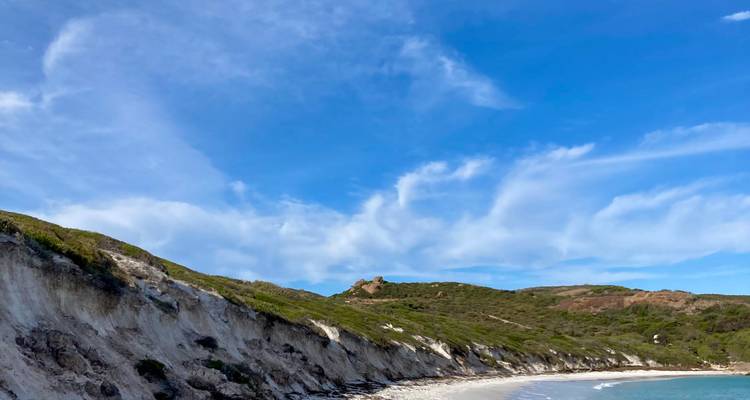 Cliffside beach with white strata and wispy cirrus clouds in a blue sky