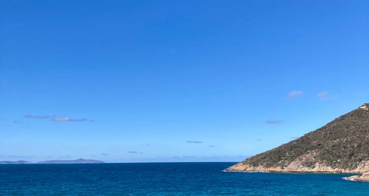 Deep blue sea with a rugged hillside headland under a clear azure sky