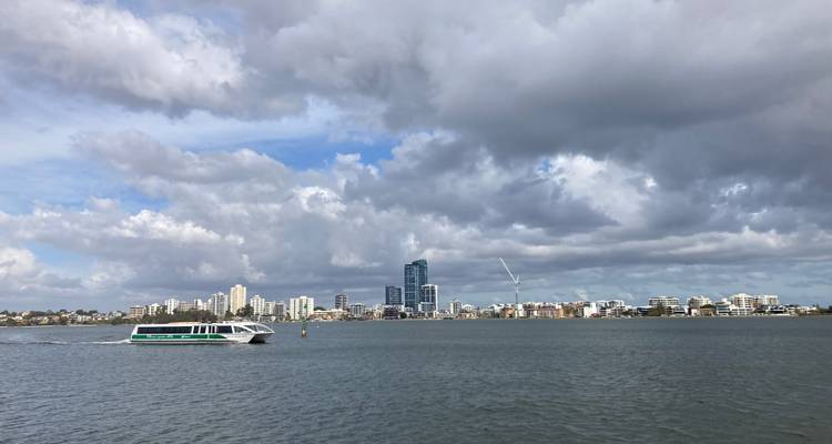 River ferry cruising past a modern waterfront skyline under dramatic clouds