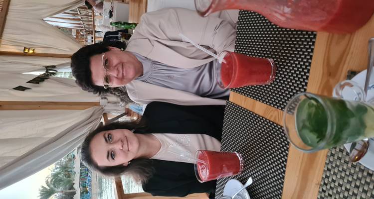 Two women seated at a wooden restaurant table with colorful drinks and patterned placemats.