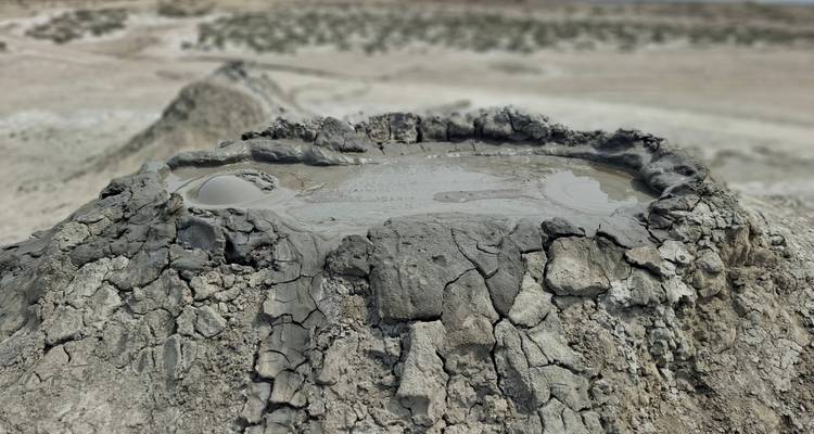 Gros plan d'un bassin de boue bouillonnante au sommet d'un petit volcan de boue dans un paysage aride