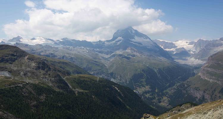 Majestic Matterhorn peak towering above sprawling alpine valleys beneath a partly cloudy sky.