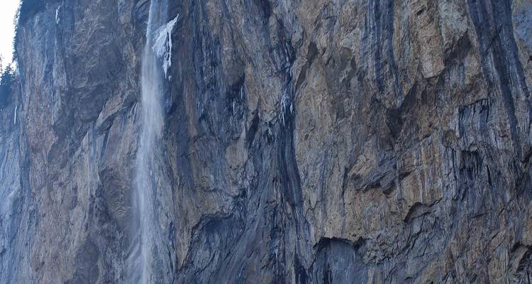 Tall, narrow waterfall plunging down a sheer rock face with dark striations.