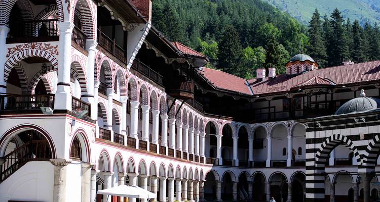 Les longues galeries voûtées du monastère de Rila entourent la cour intérieure tranquille avec des collines boisées en arrière-plan.