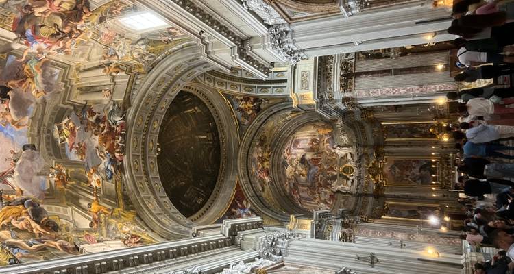 Interior de iglesia Barroca lujosamente decorada con techos frescos que se elevan hacia el cielo y columnas de mármol llenas de visitantes.
