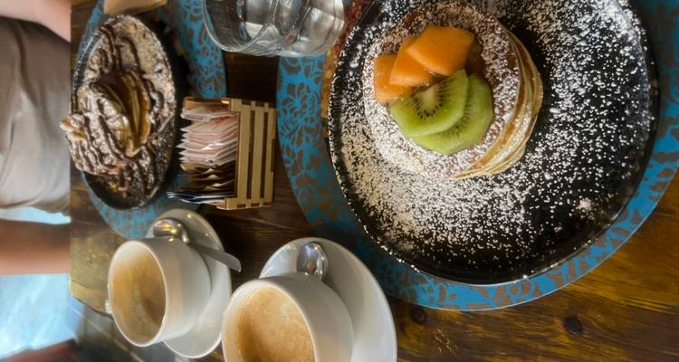 Mesa servida con capuchinos y pilas de panqueques cubiertos de azúcar en polvo y frutas frescas.