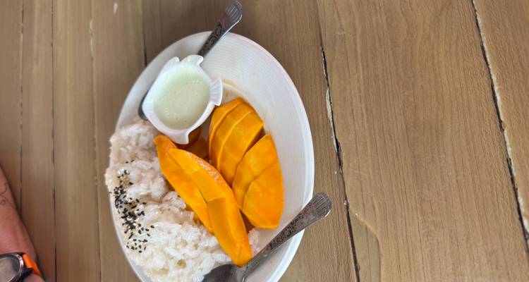 A plate of mango sticky rice dessert with coconut cream served on a wooden table.