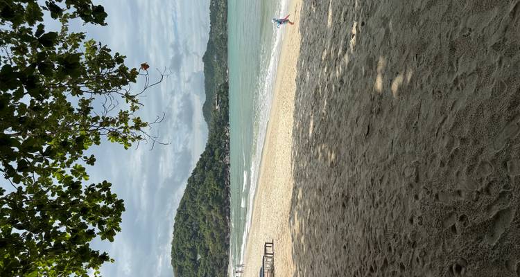 A wide sandy beach with gentle waves and a child playing near the shoreline under a partly cloudy sky.
