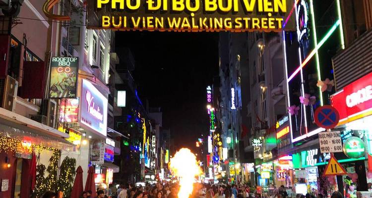 Bustling Bui Vien Walking Street at night with neon lights and street performer breathing fire.