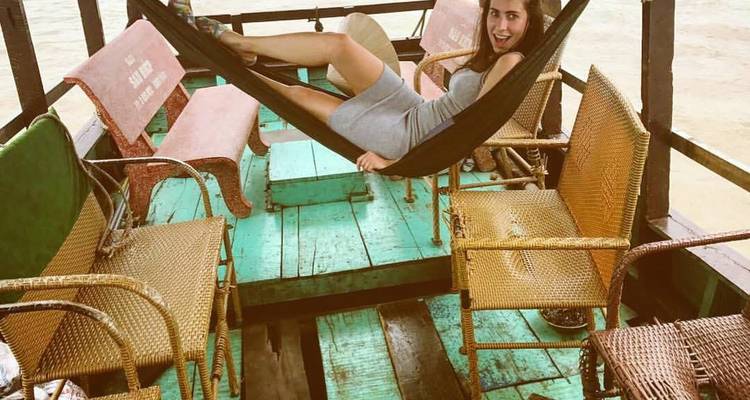 Woman relaxing in a hammock aboard a rustic wooden boat on muddy river waters.