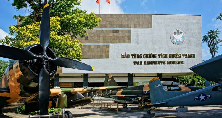 Exterior of War Remnants Museum with military aircraft displayed in front and Vietnamese flags.