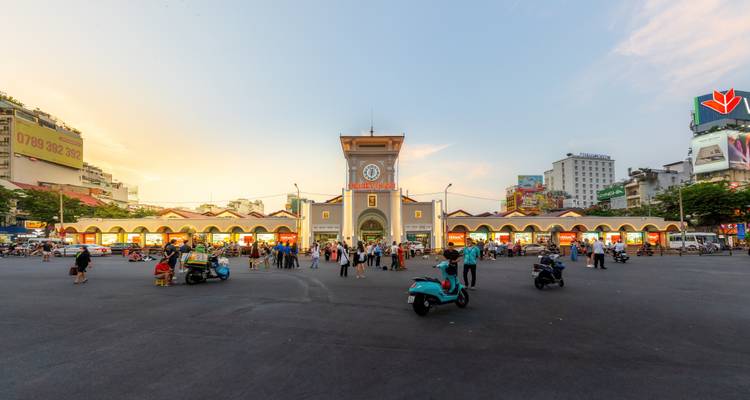 Plaza amplia frente al Mercado Ben Thanh con scooters y peatones a la hora dorada.