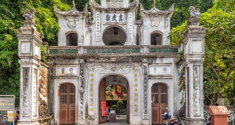 Puerta de templo blanco histórica adornada con tallados intrincados y caracteres chinos, rodeada de exuberante vegetación.