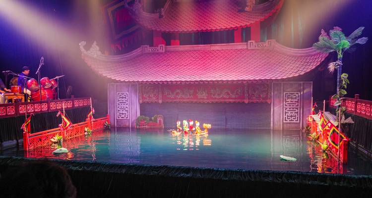 Escenario tradicional de teatro de marionetas acuáticas vietnamitas con iluminación vibrante y marionetas actuando en el agua.