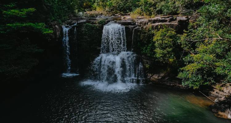 Twin cascade waterfall plunging into a dark pool within dense jungle.