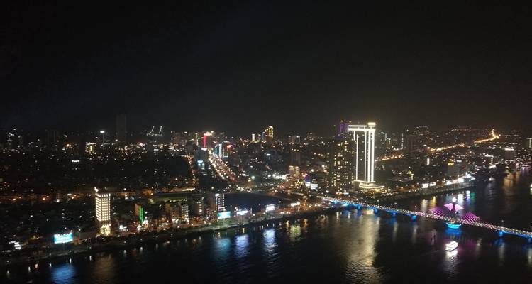 Night aerial view of Da Nang city skyline with illuminated bridges and reflections on the Han River.