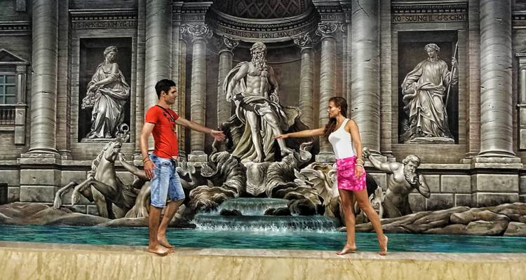 Two people pose as if stepping into the Trevi Fountain illusion surrounded by classical statues.