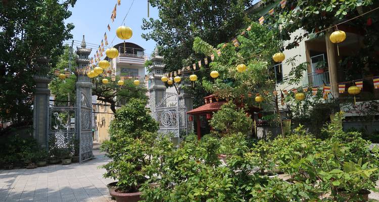 Temple entrance draped with yellow lanterns and surrounded by leafy plants in bright sunlight.