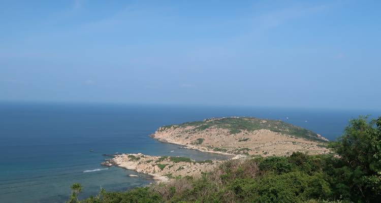 Clear coastal headland jutting into deep blue sea under a cloudless sky, viewed from above.