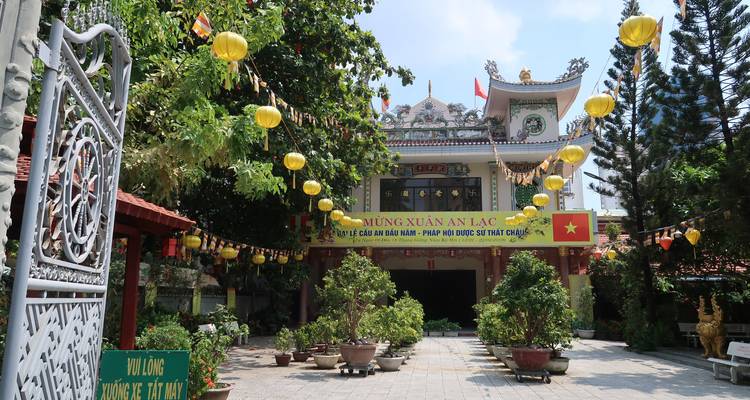 Courtyard of a Vietnamese pagoda decorated with yellow lanterns, banners and bonsai pots.