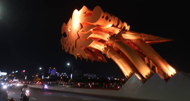 Close-up night view of the illuminated orange dragon head of Da Nang’s Dragon Bridge over roadway traffic.