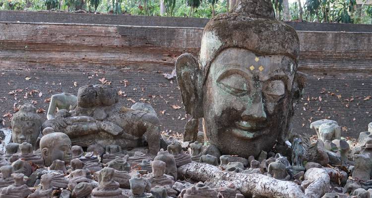 Verwitterter Buddhakopf und dutzende kleine Steinfigarinen, die auf dem Gelände eines antiken Ziegeltempels verstreut sind.