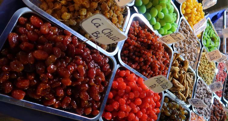 Bunte Tabletts mit kandiertem Obst und Snacks, ordentlich angeordnet an einem vietnamesischen Marktstand.