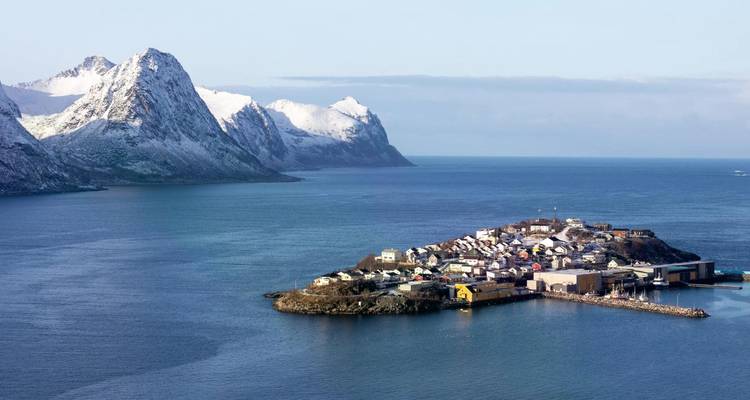 Une petite communauté insulaire se situe dans un fjord turquoise entouré de pics enneigés imposants.