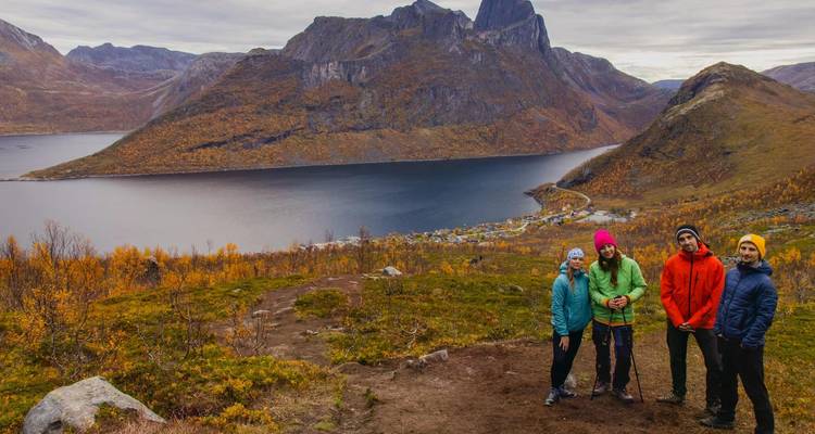 Quatre randonneurs posent sur un versant de colline dominant un fjord calme et une vallée aux couleurs automnales.