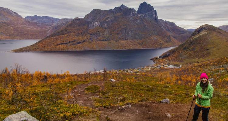 Un randonneur souriant avec des bâtons de trekking profite d'une vue panoramique sur les montagnes et les fjords en automne.