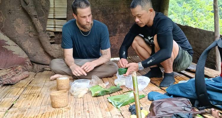 Gids en trekker zitten op een bamboevloer en bereiden voedsel voor dat in bananenbladen is gewikkeld in een rustieke schuilplaats.