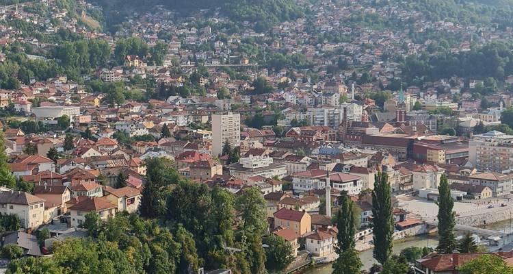 Vue panoramique des quartiers aux toits rouges s'étendant à travers les collines et les vallées verdoyantes de Sarajevo.